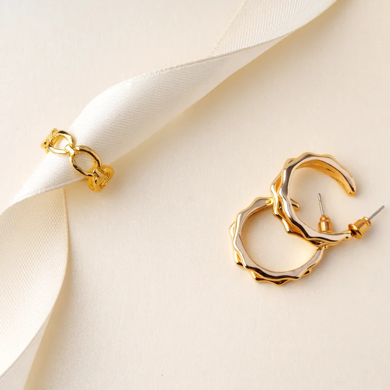 Gold hoop earrings arranged on cream fabric with a white ribbon