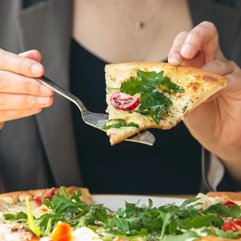 A woman lifting a slice of rocket pizza from the pan with a fork
