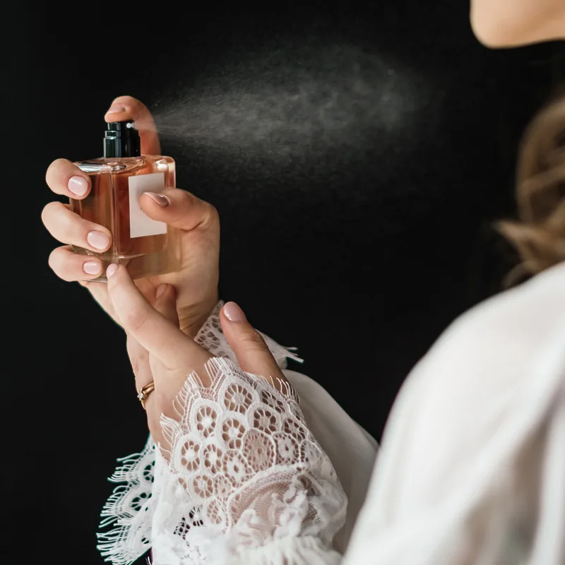A woman spraying perfume, photographed against a dark background