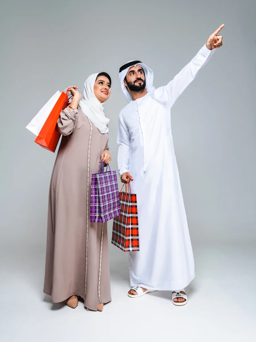 A couple in traditional Emirati dress carrying shopping bags, one of them pointing