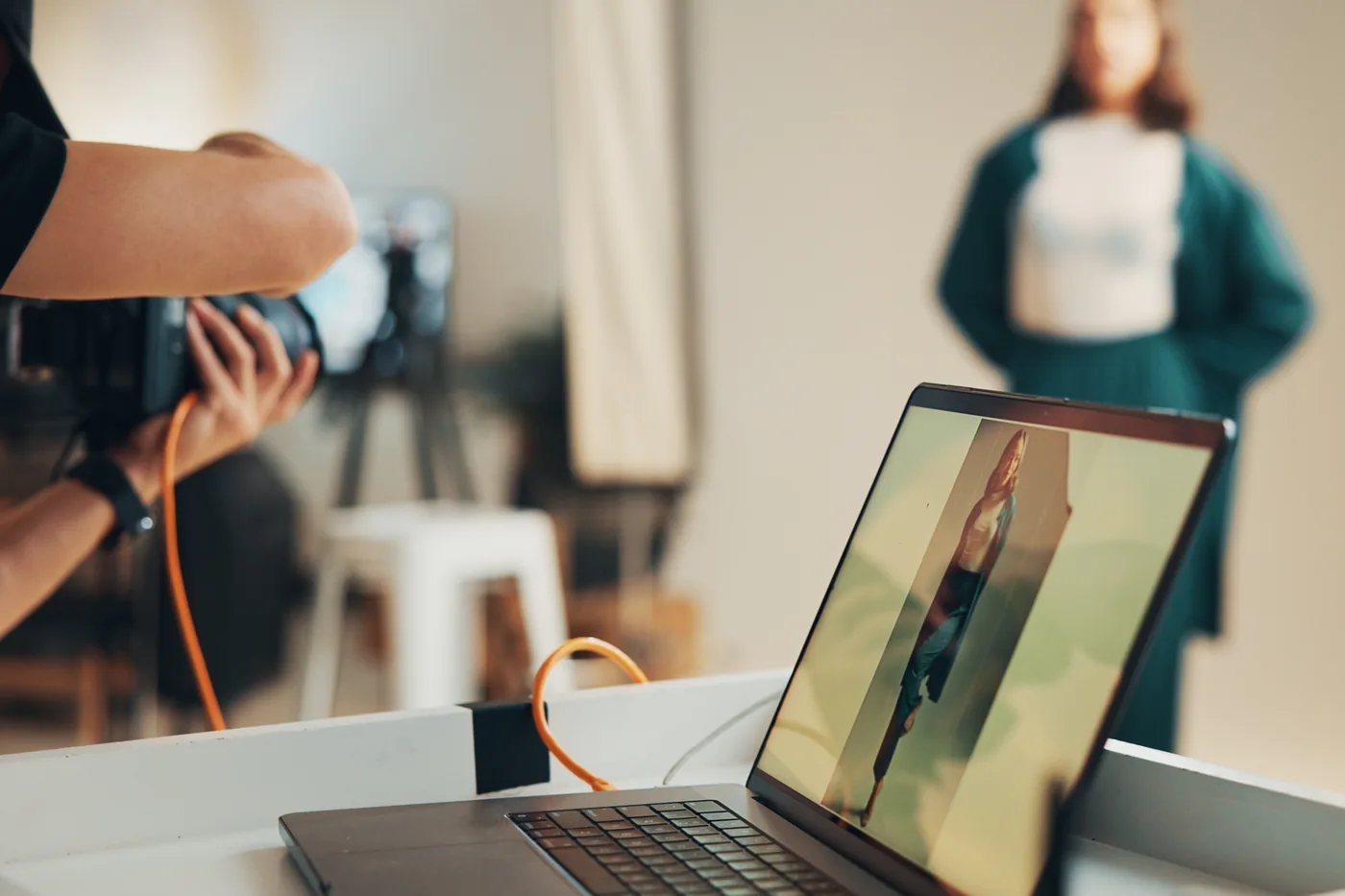 A photographer shooting a model in a bright studio, the frame showing on a tethered laptop