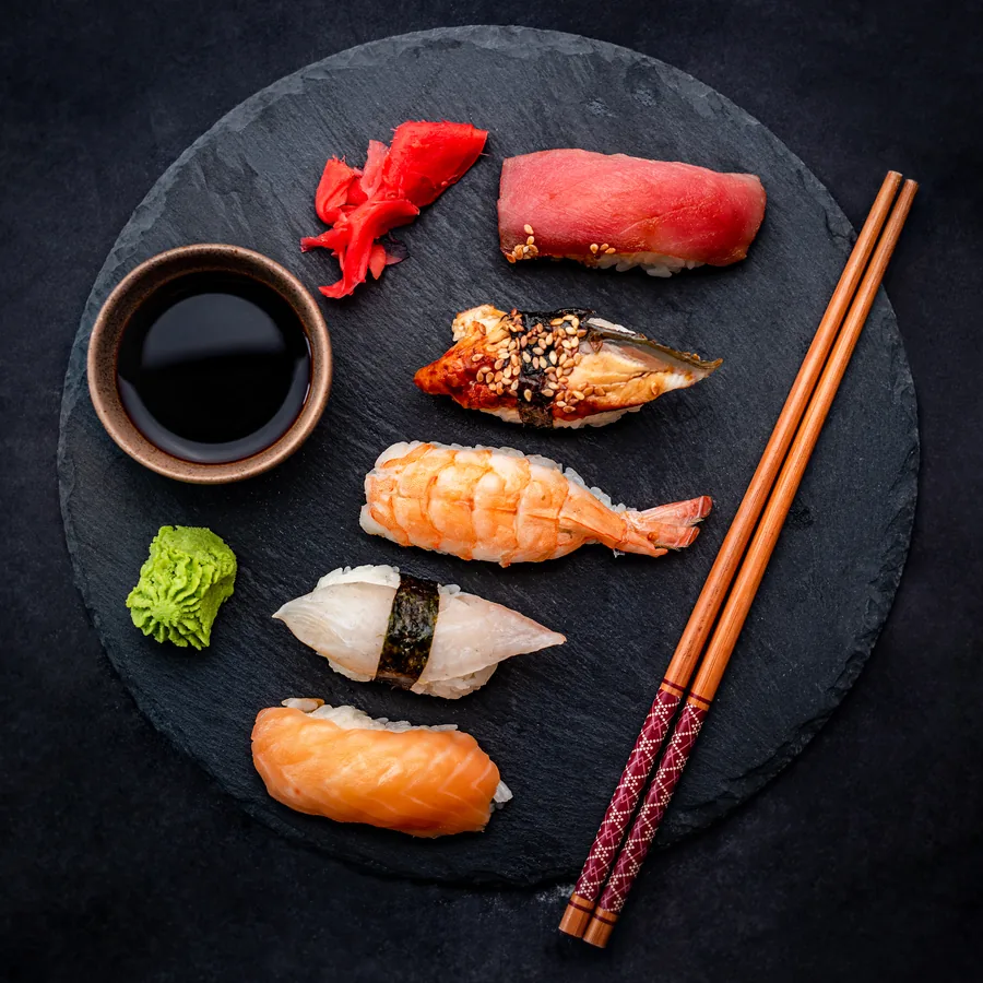 A sushi selection on a round slate plate with soy, wasabi and chopsticks